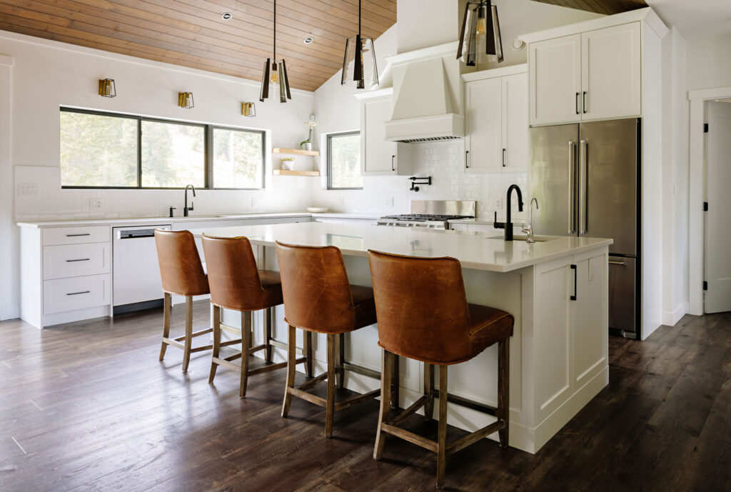Image showing country kitchen with white cabinetry, large island additional sink and lots of counter space. There is a breakfast bar with four leather bar height chairs.