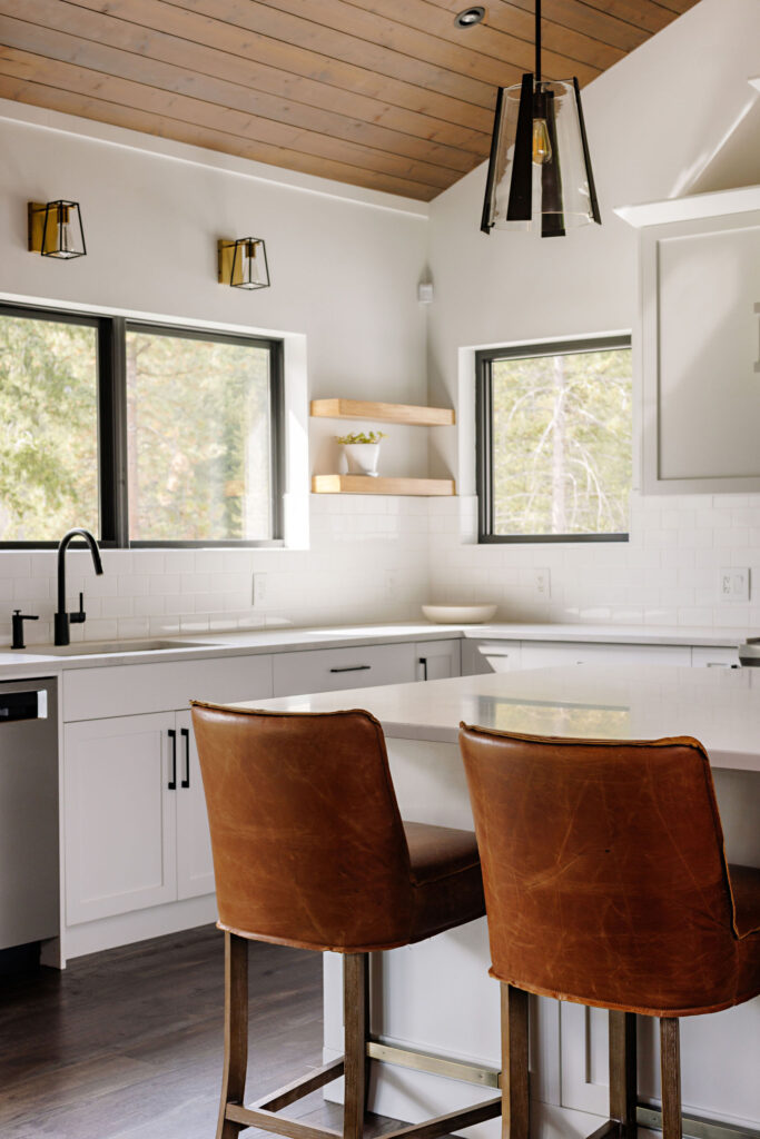 Image showing country kitchen with white cabinetry, large island additional sink and lots of counter space. There is a breakfast bar with four leather bar height chairs.