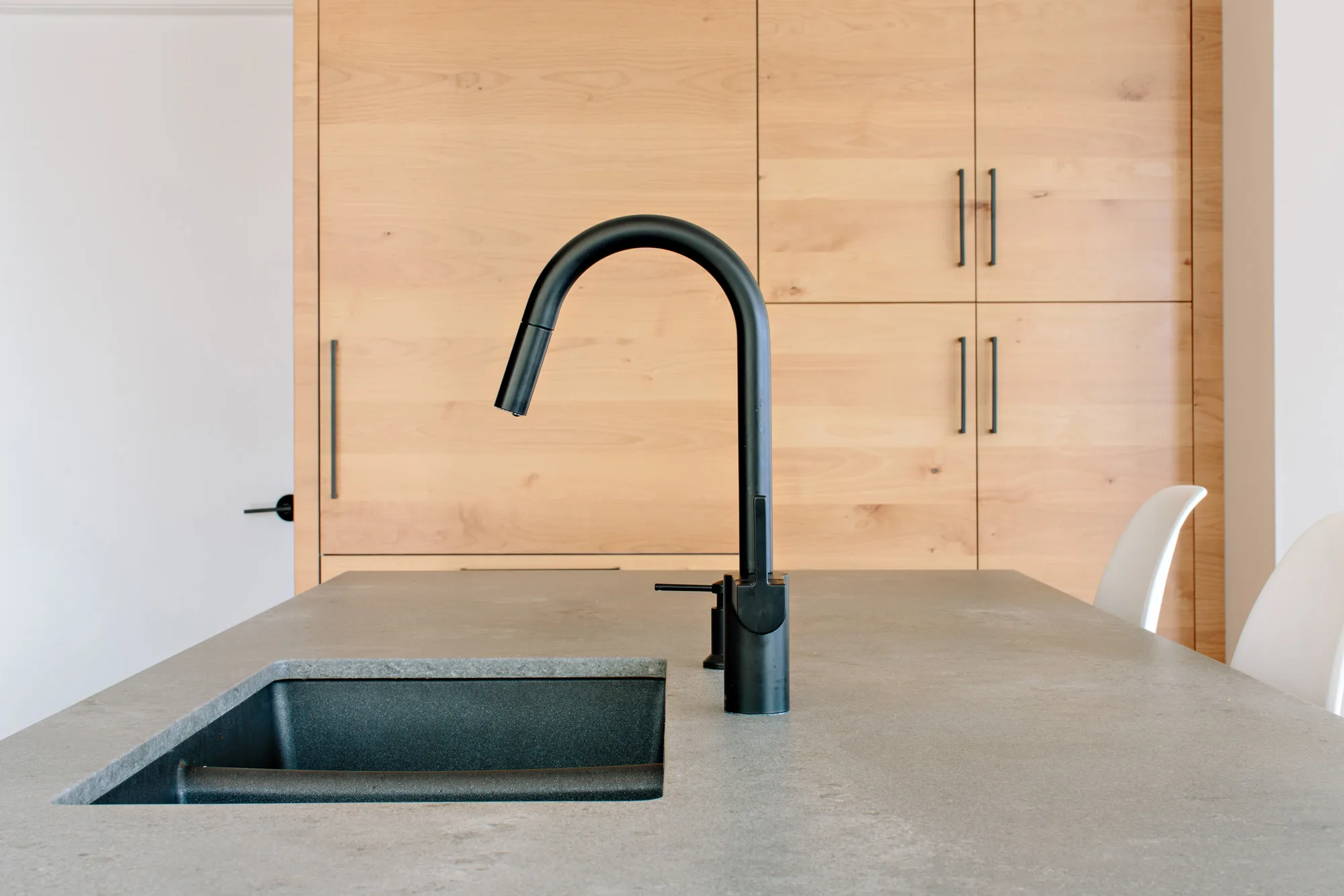 Image showing kitchen island details with a Caesarstone countertops, black sink and faucet. There are natural wood cabinets in the background. Built by Whitfield Homes