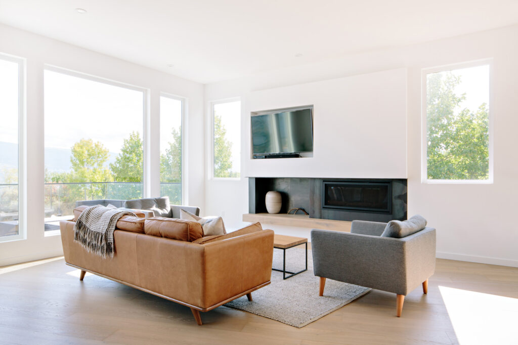 Image of a livingroom with large windows, raw steel fireplace accents and mid-century modern furniture. Built by Whitfield Homes.