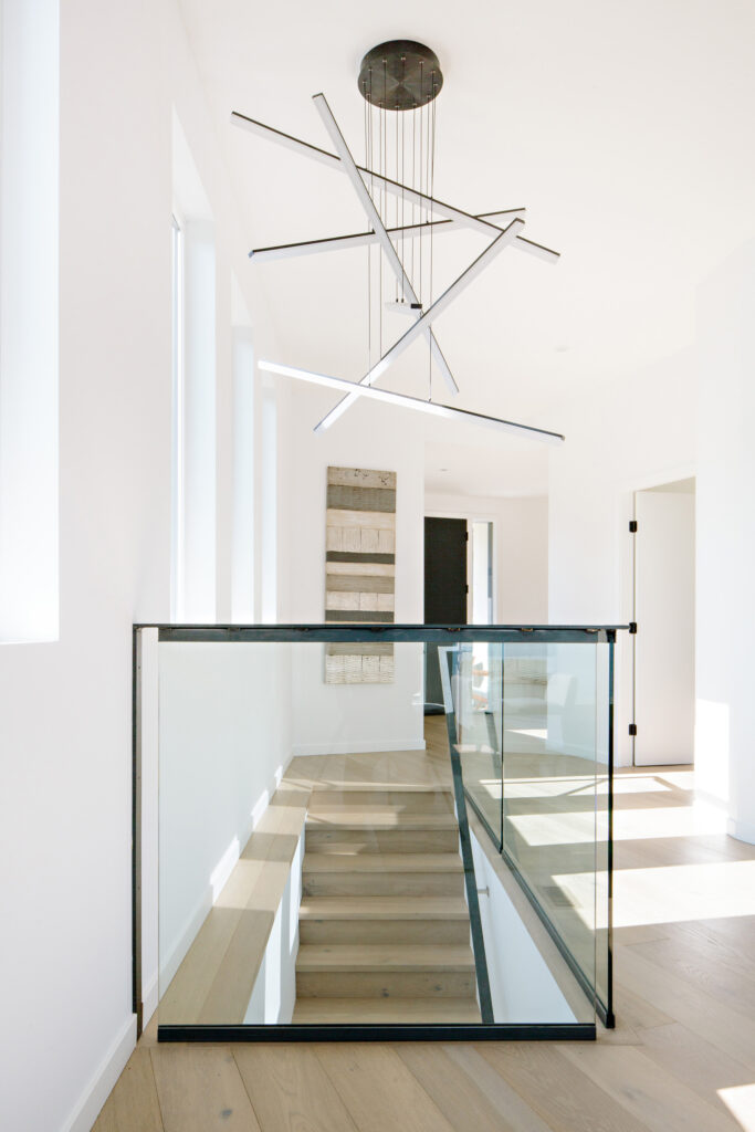 Image of the stairway with glass and raw steel railing. There is lots of natural light and a modern light fixture. Built by Whitfield Homes.