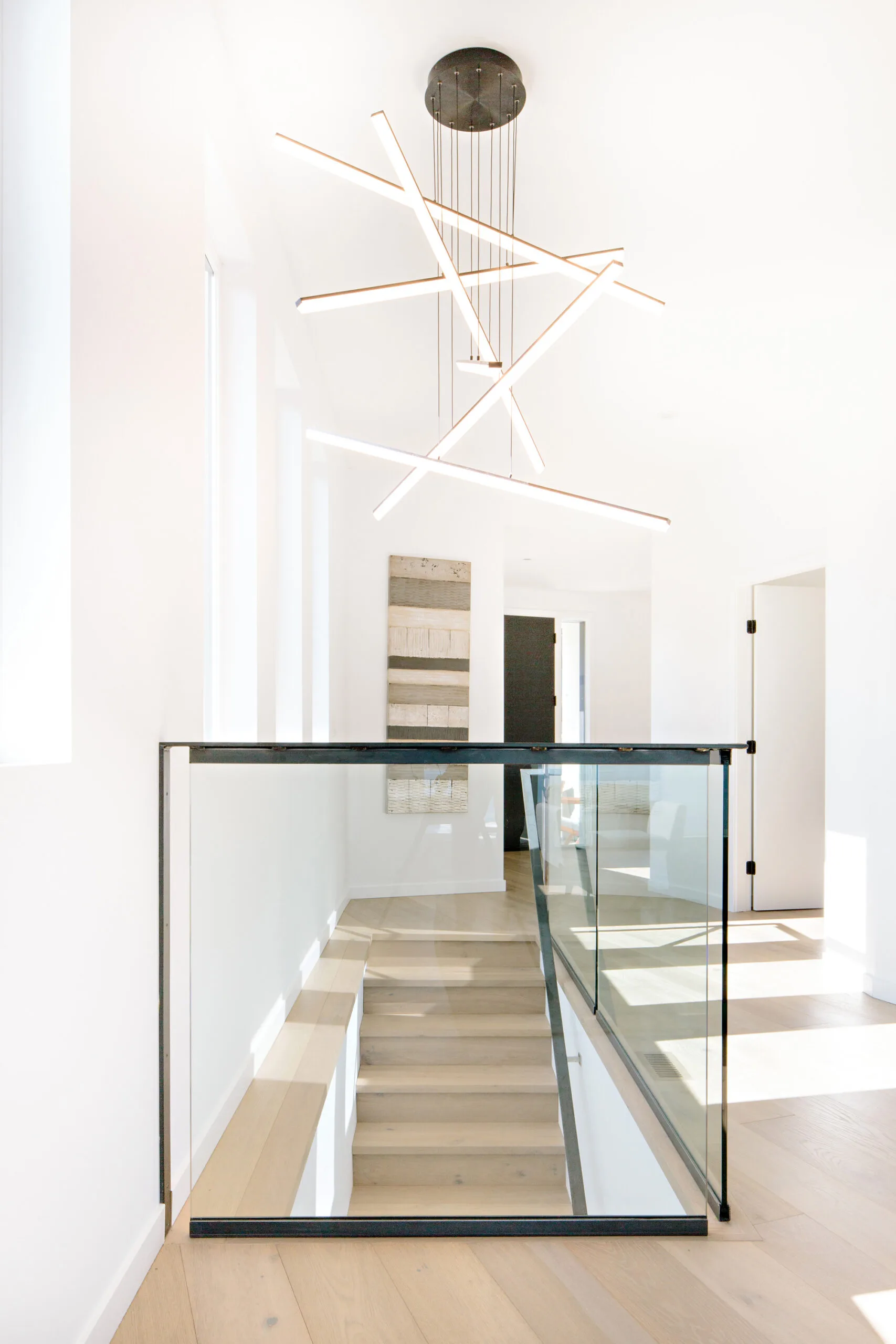 Image of the stairway with glass and raw steel railing. There is lots of natural light and a modern light fixture. Built by Whitfield Homes.