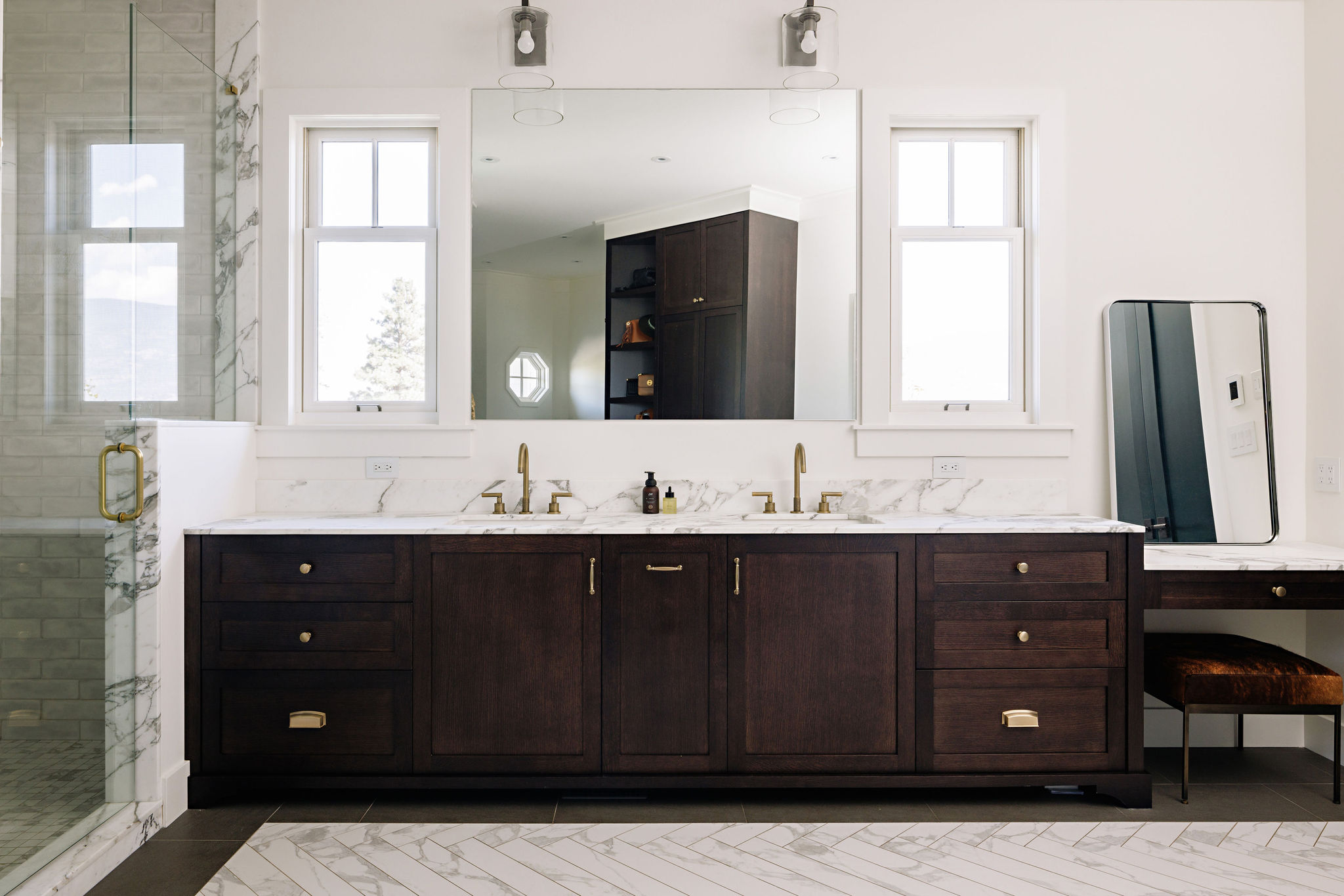 Image of a bathroom vanity with custom dark wood cabinetry, marble countertops and double sinks.