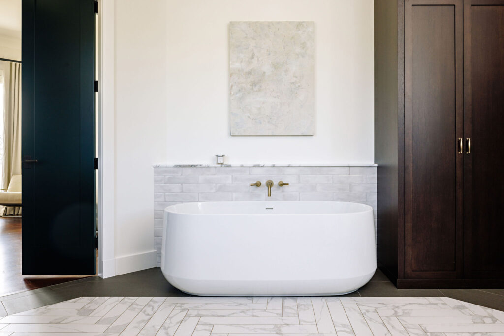 Imae of a white freestanding tub with a tall dark wood cabinet beside it. There is a doorway into the master bedroom on the left.