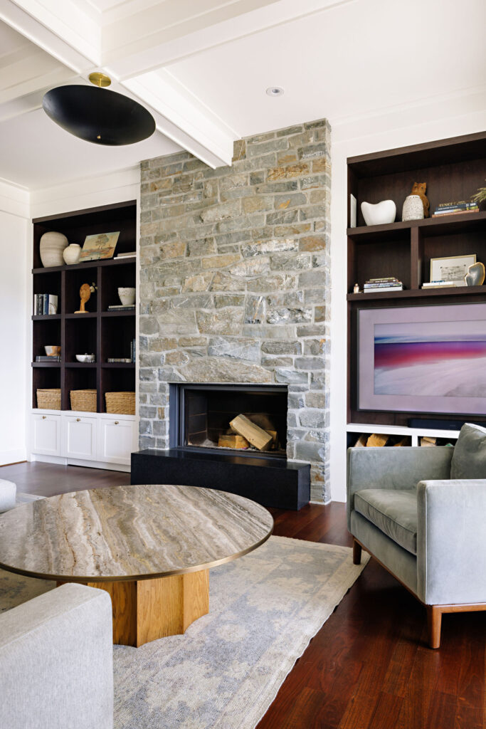 Image showing a fireplace with a natural stone surround. There are custom built-ins on either side of the fireplace. The ceiling is white and features large beams and an overhead light.