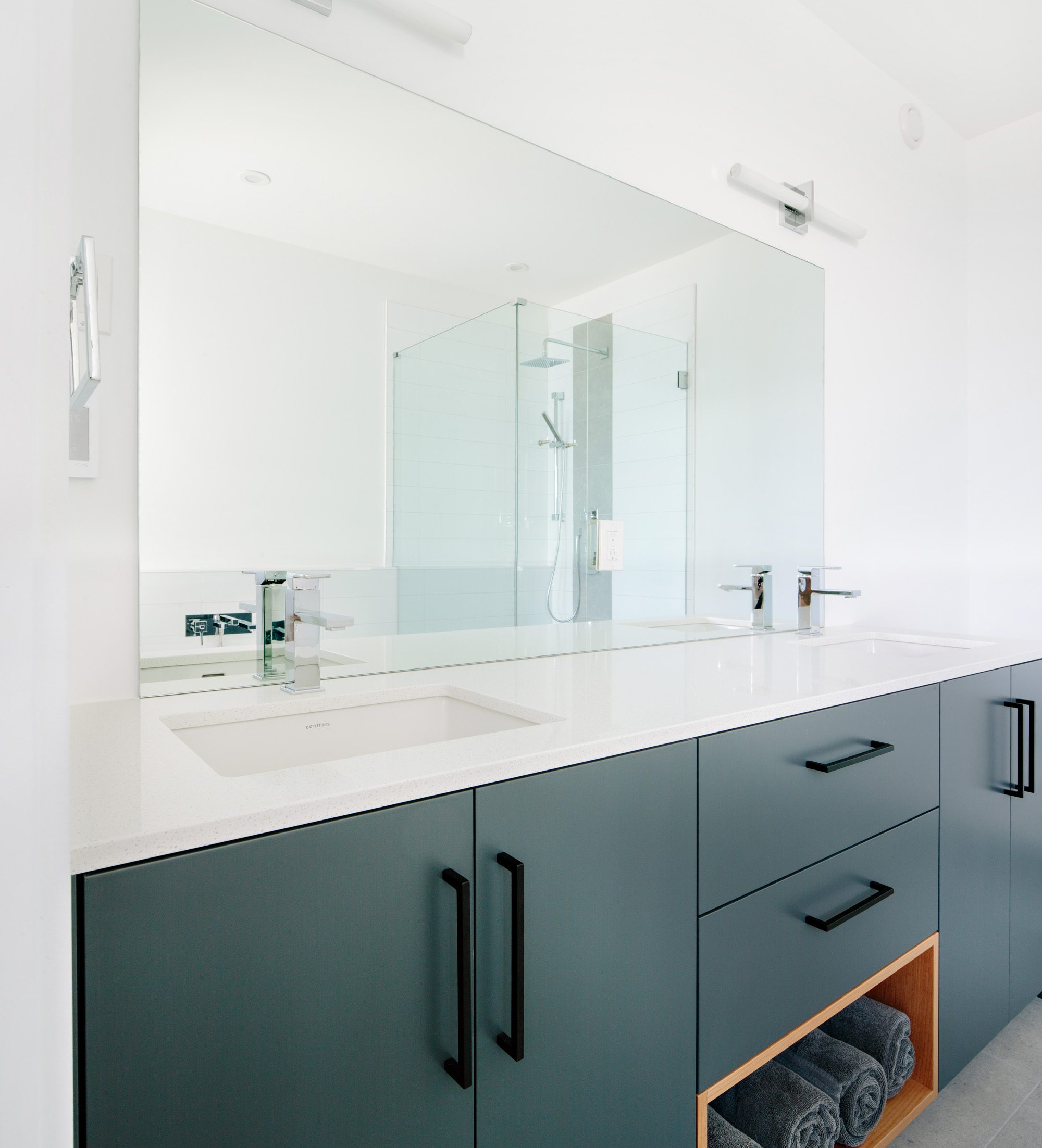Image of a bathroom vanity with large mirror, double sinks and custom grey cabinets with white countertops. Built by Whitfield Homes